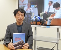 刊行の意義を語る箕浦暁雄教授。背後の写真は5月の出版記念イベントの様子