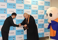 目録を手渡す一隅を照らす運動理事長代理の荒樋総本部長