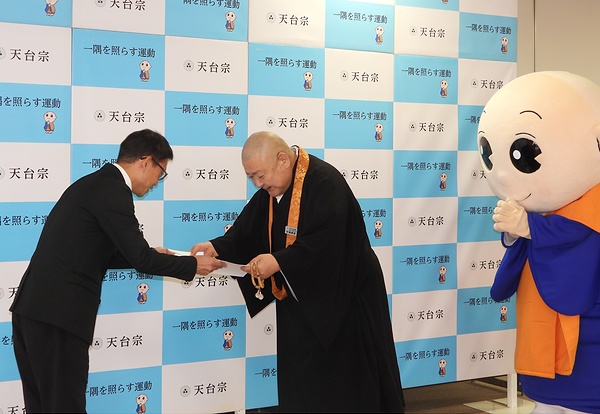 目録を手渡す一隅を照らす運動理事長代理の荒樋総本部長