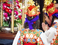 誕生仏に甘茶をそそぎ、はにかみながら手を合わせる稚児