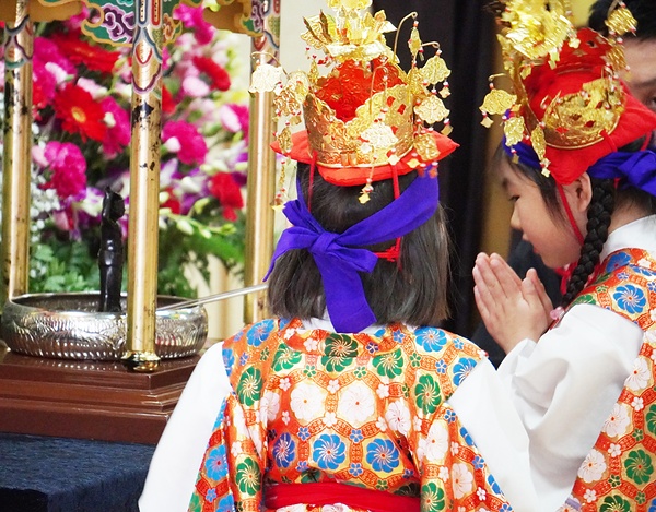 誕生仏に甘茶をそそぎ、はにかみながら手を合わせる稚児