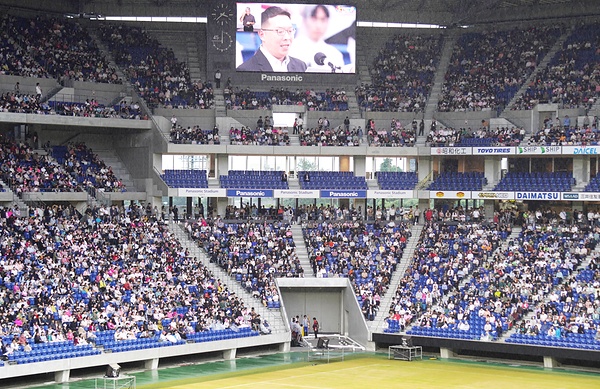 大勢の青年が集まった会場（モニターは挨拶する前田青年部長）