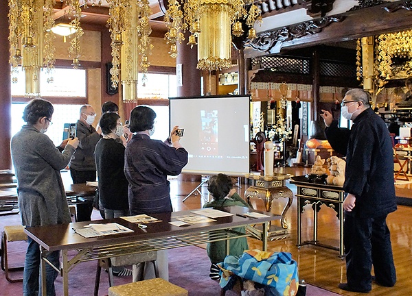 スマホのカメラで仏像を撮影する参加者と伊藤住職（右端）