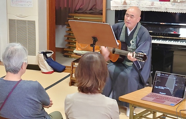 ピアノの生伴奏で歌謡曲を楽しむ集いでギターを手に熱唱する平田住職